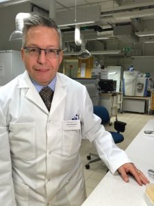 Picture of Jonas Bergquist in the lab. He has a warm smile and is wearing a white lab coat with his name tag on it.