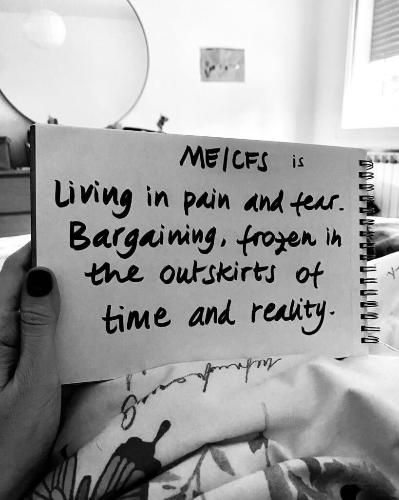 Ali is holding a sign that reads: “ME/CFS is living in pain and fear. Bargaining, frozen in the outskirts of time and reality.”