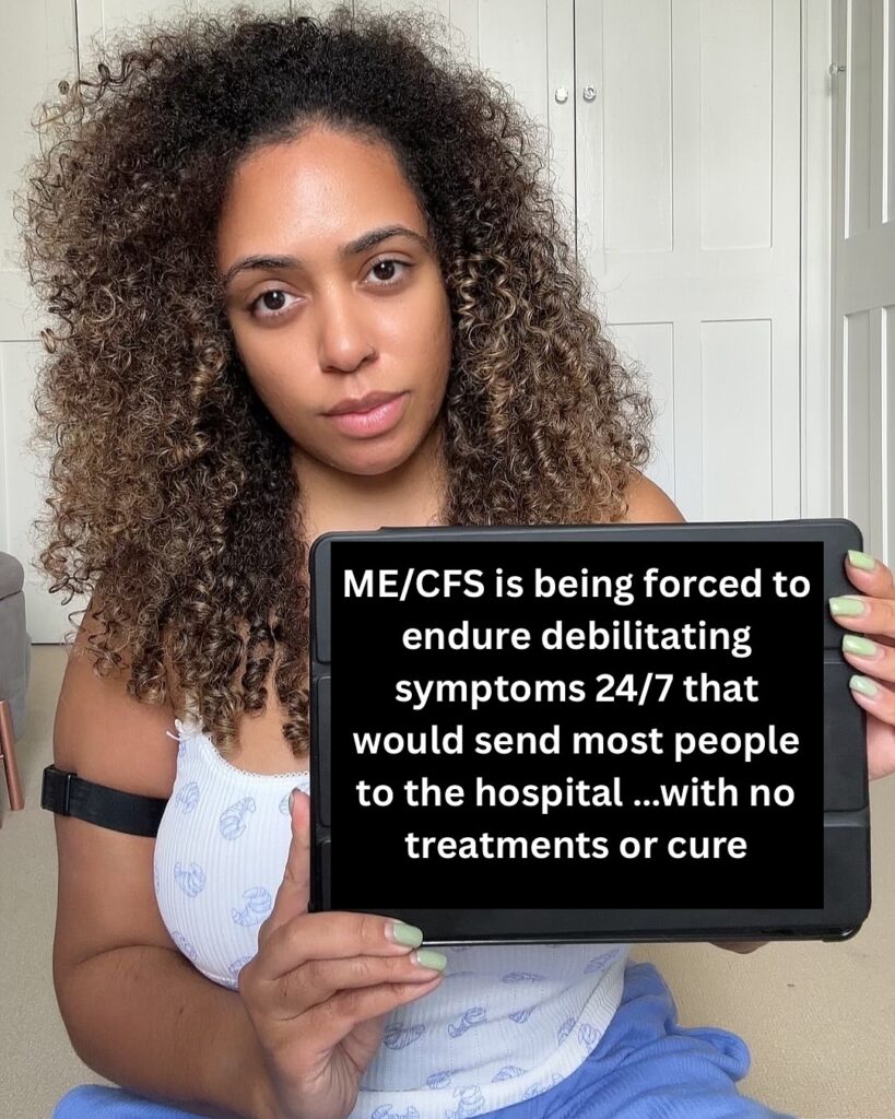 Shan is holding a sign that reads: ME/CFS is being forced to ensure debilitating symptoms 24/7 that would send most people to the hospital..with no treatments or cure.