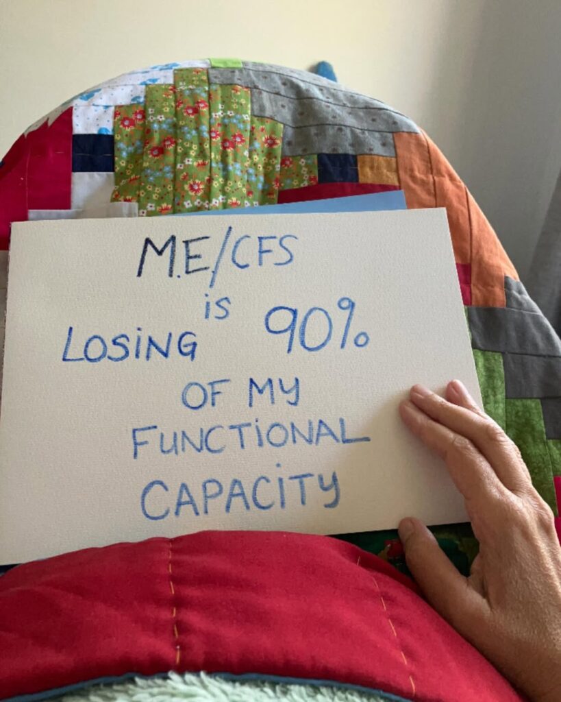 Bridie is holding a sign that reads: ME/CFS is losing 90% of my functional capacity.